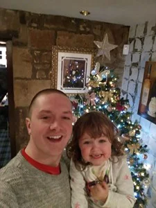 man living with an Ileostomy posting with a child in front of a Christmas tree